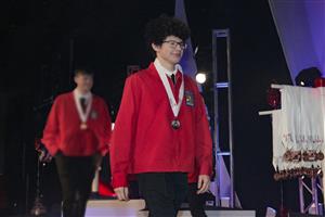 Abner on stage receiving silver medal in red jacket 