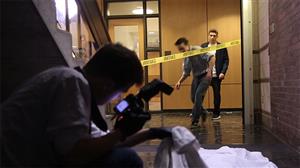 detective takes a photo of the scene while two investigators duck under caution tape 