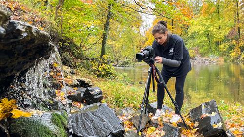 Student operates camera on a river bank